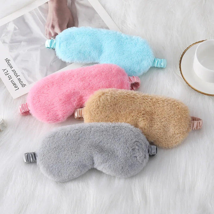 Quattro mascherine per dormire in peluche colorate su sfondo bianco, ideali per il relax e il sonno. Accessori morbidi e confortevoli.