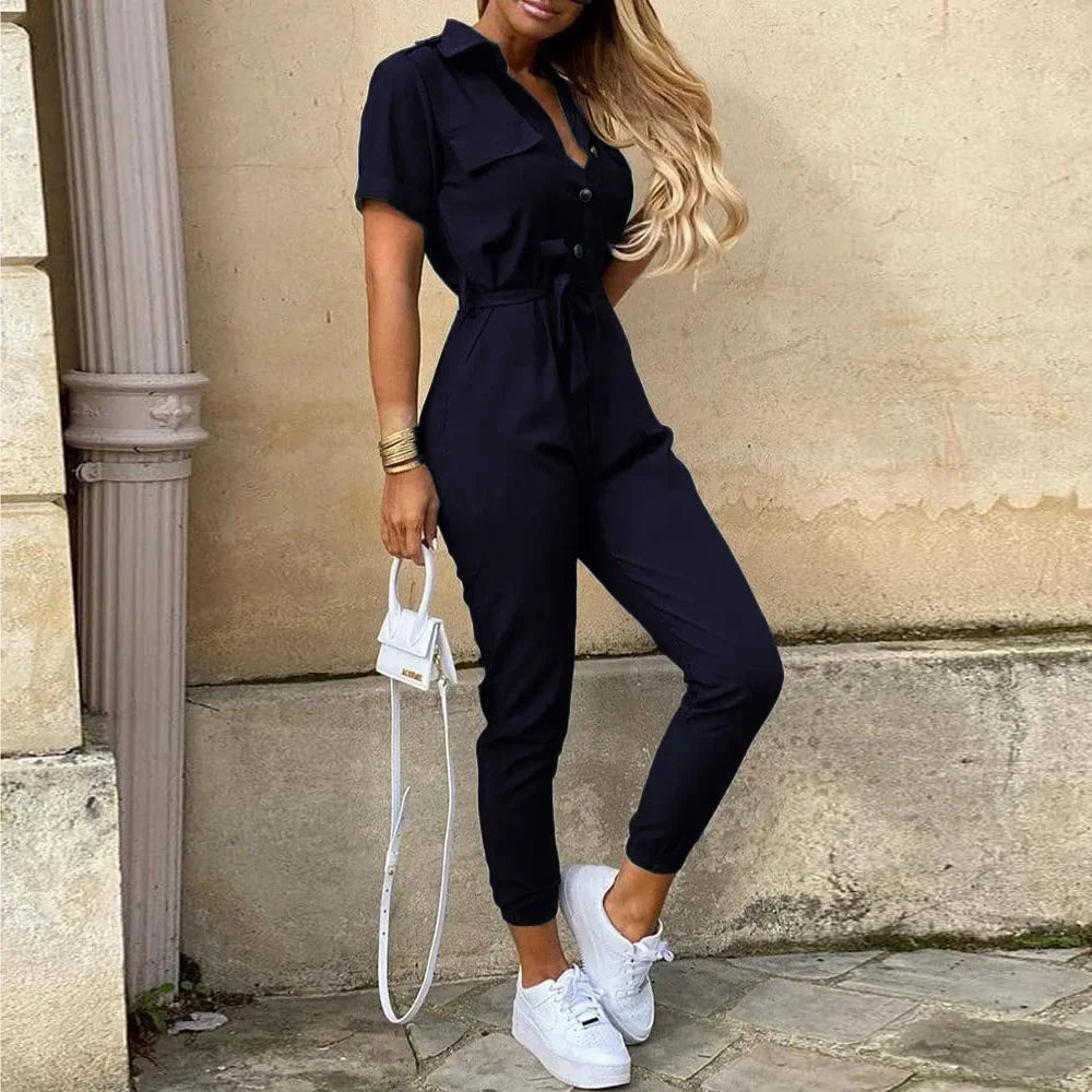 Donna con tuta nera elegante, maniche corte, abbinata a scarpe bianche e borsa a tracolla. Look casual chic per moda femminile estiva.