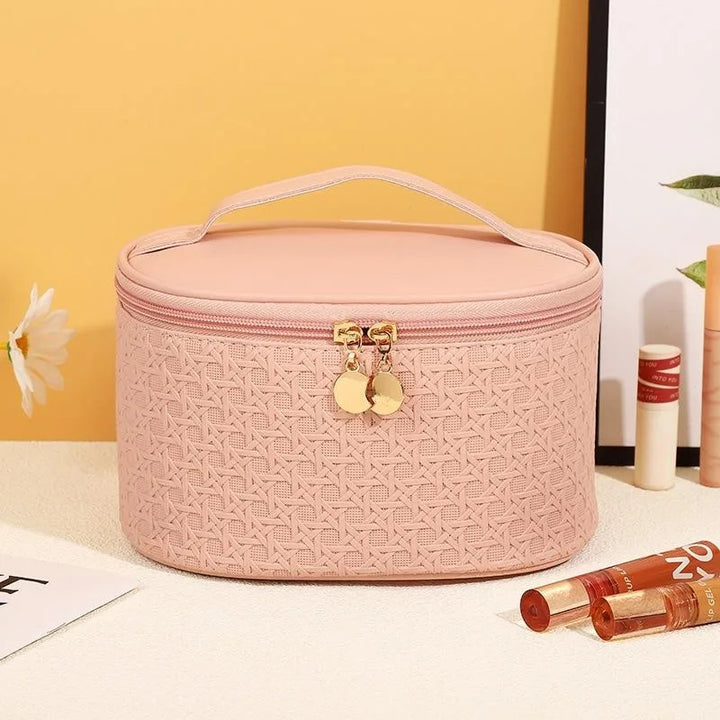 Astuccio cosmetico rosa con motivo intrecciato, chiusura a zip dorata, manico superiore. Accessorio elegante per trucco e bellezza.
