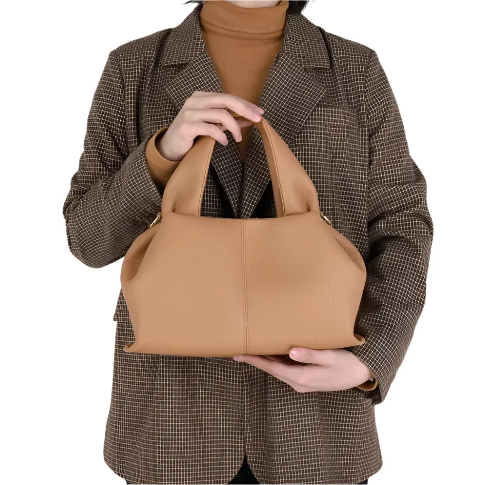Donna con cappotto a quadri tiene borsa a mano beige in pelle, elegante e moderna. Accessorio moda femminile, perfetto per ogni occasione.