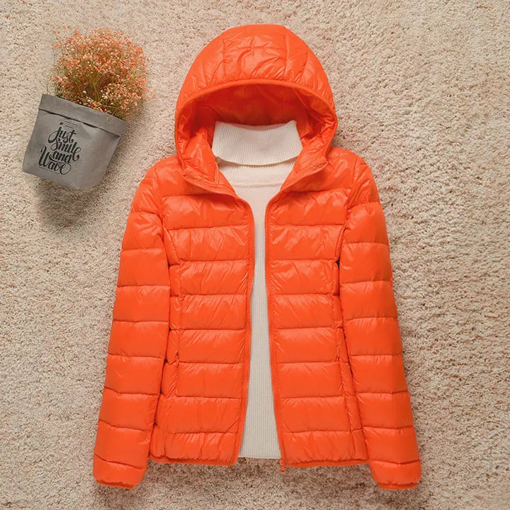 Giacca invernale arancione con cappuccio, imbottita, su sfondo beige. Moda donna, abbigliamento caldo, giacca trapuntata leggera.