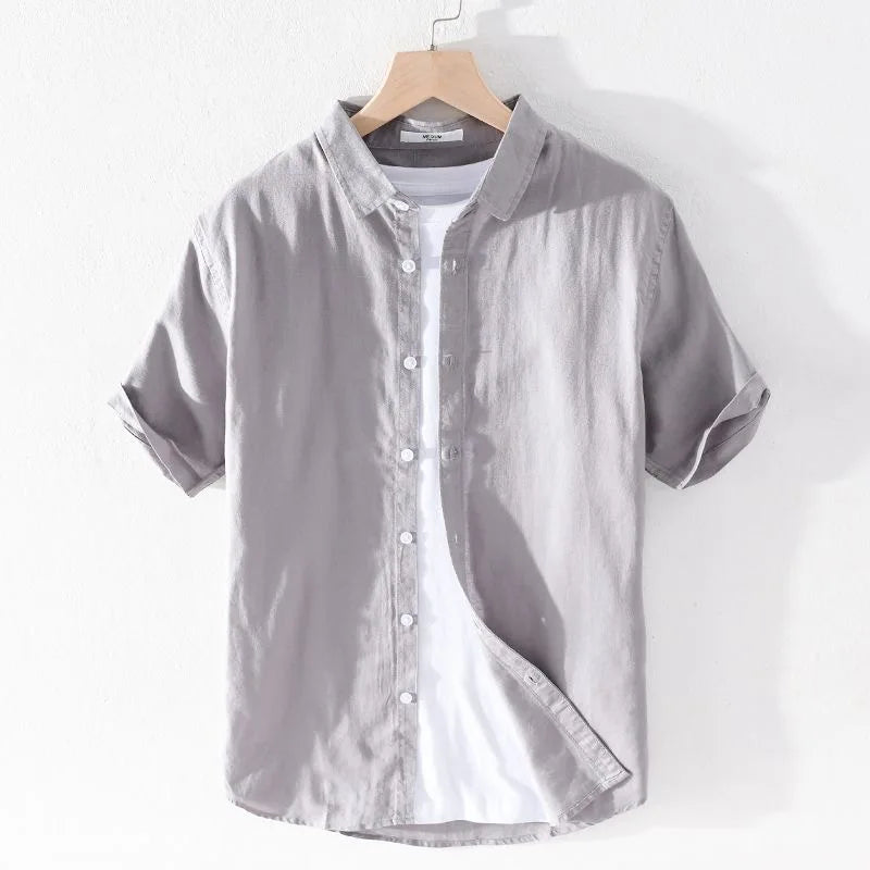 Camicia grigia a maniche corte in cotone, stile casual, con colletto classico e bottoni bianchi, appesa su gruccia di legno.