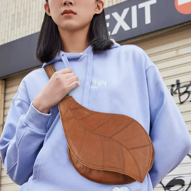 Giovane con felpa viola indossa borsa a tracolla marrone a forma di foglia. Moda urbana, accessori unisex, stile casual.