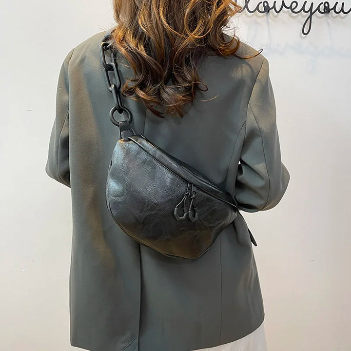 Giacca elegante grigia con borsa a tracolla in pelle nera, catena decorativa, indossata da donna di spalle. Moda autunno, accessori di tendenza.