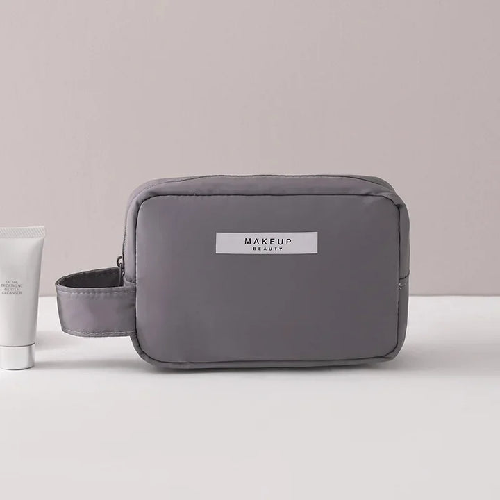 Borsa trucco grigia con manico, design minimalista, accanto a un tubetto bianco. Ideale per cosmetici, viaggio, organizzazione beauty.