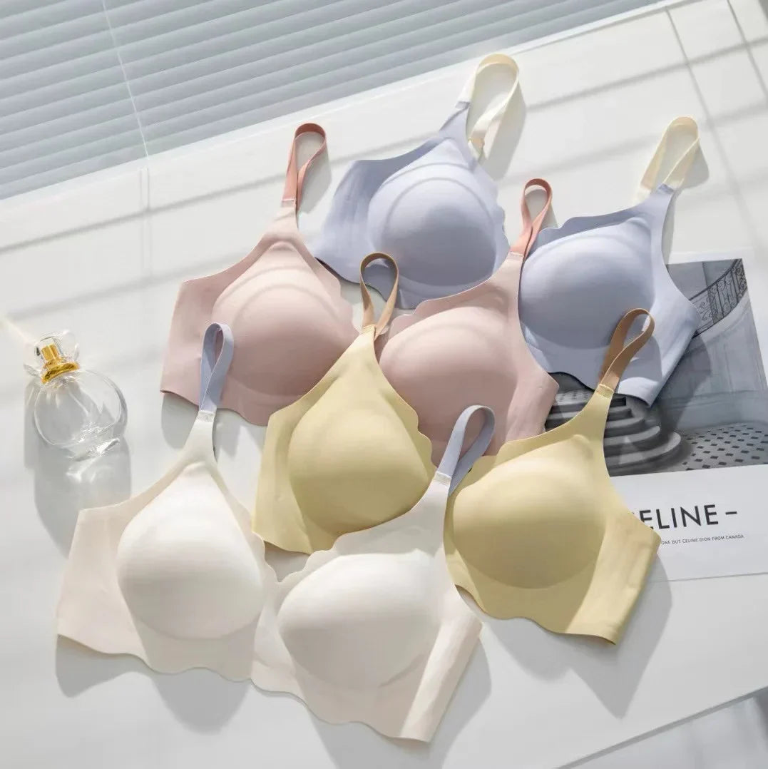 Reggiseni senza cuciture in vari colori pastello su sfondo bianco, con bottiglia di profumo. Intimo comodo e alla moda per donna.