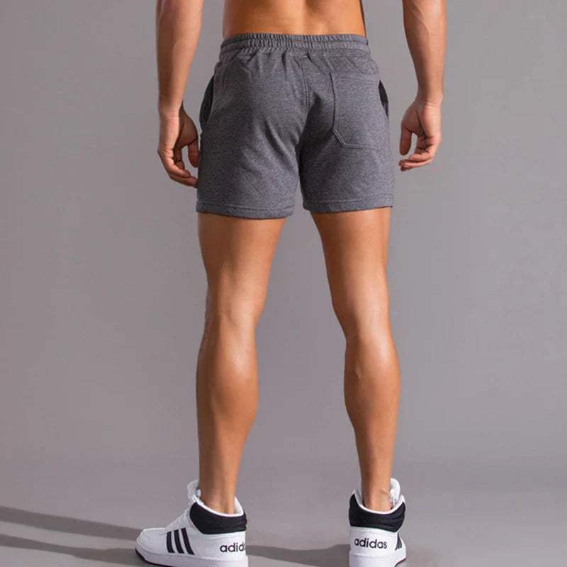 Shorts sportivi uomo grigi, vista posteriore, tessuto traspirante, ideali per palestra e fitness. Indossati con scarpe Adidas bianche e nere.
