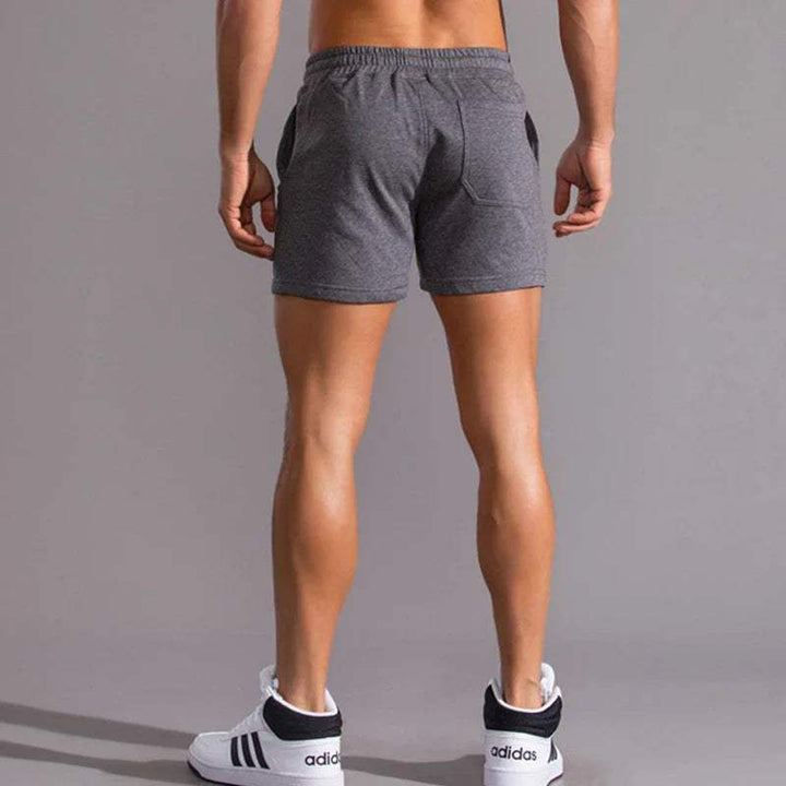Shorts sportivi uomo grigi, vista posteriore, tessuto traspirante, ideali per palestra e fitness. Indossati con scarpe Adidas bianche e nere.