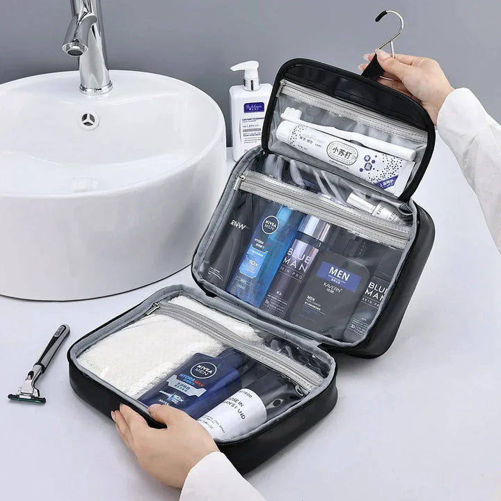 Astuccio da viaggio nero aperto con prodotti per l'igiene maschile, appeso vicino a un lavandino bianco. Include shampoo, deodorante e rasoio.