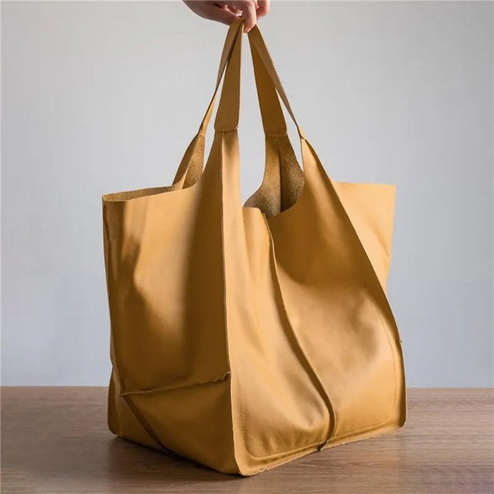 Borsa shopper in pelle gialla su tavolo di legno, design minimalista, manici lunghi, ideale per shopping e uso quotidiano. Accessorio moda elegante.