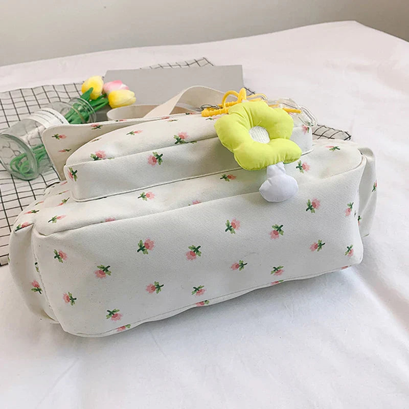 Borsa a tracolla bianca con stampa floreale rosa, decorata con ciondolo giallo. Design elegante e femminile, perfetta per la moda casual.