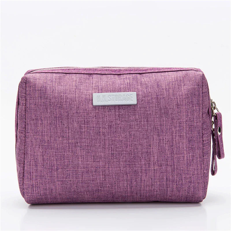 Astuccio da viaggio viola in tessuto, con chiusura a zip e etichetta frontale. Ideale per organizzare accessori e cosmetici.