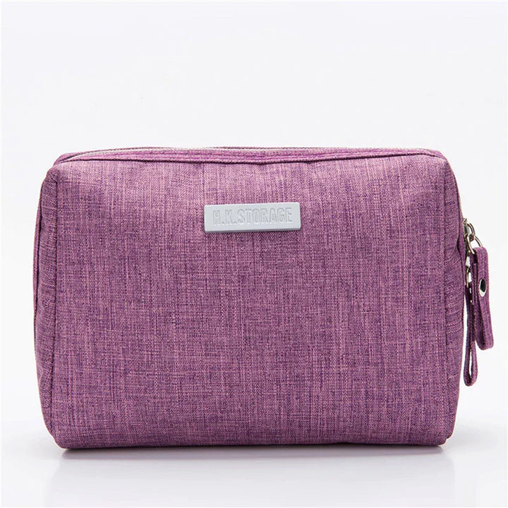 Astuccio da viaggio viola in tessuto, con chiusura a zip e etichetta frontale. Ideale per organizzare accessori e cosmetici.