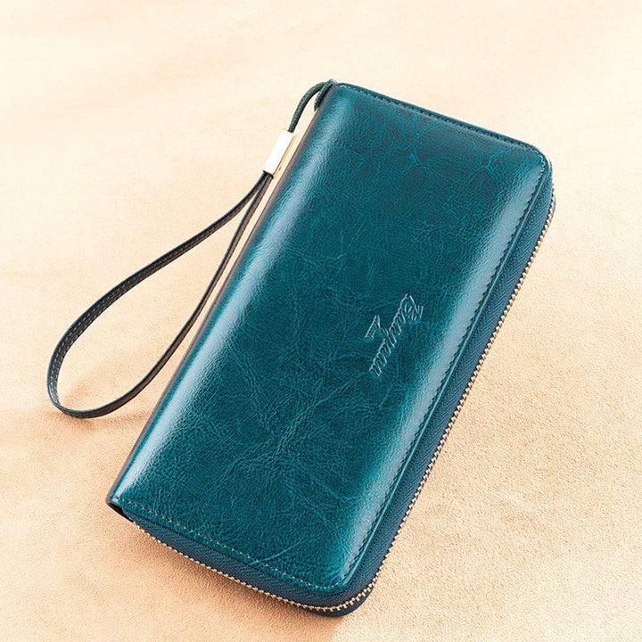 Portafoglio in pelle verde scuro con cerniera, cinturino da polso e logo inciso. Accessorio elegante per uomo e donna, ideale per regali.
