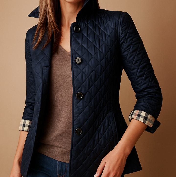 Giacca trapuntata blu scuro da donna, con colletto rialzato e polsini a quadri, abbinata a maglia marrone e jeans. Moda autunnale elegante.