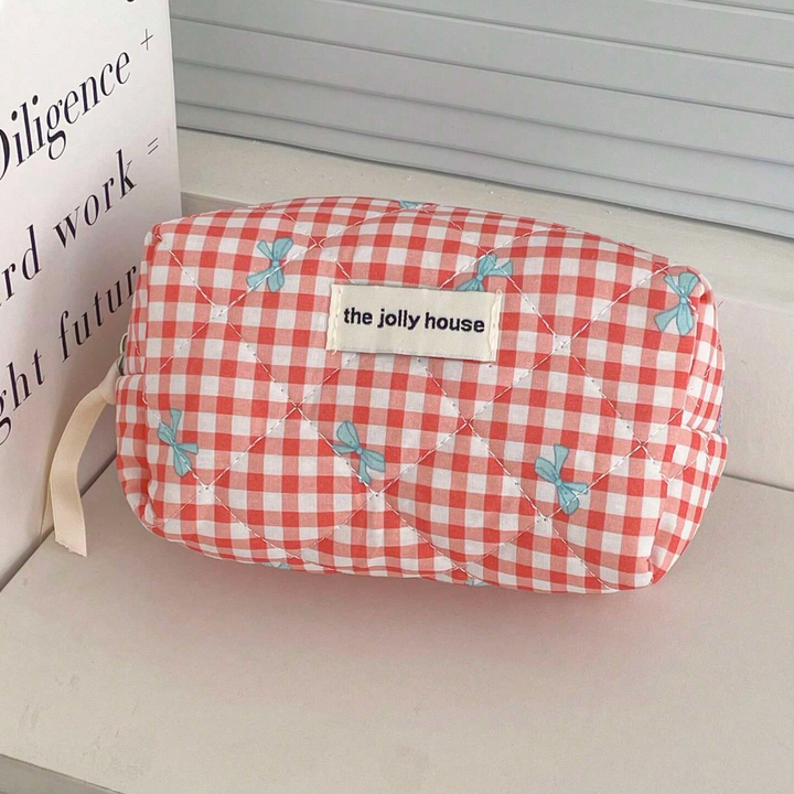 Astuccio cosmetico trapuntato a quadretti rossi e bianchi con fiocchi blu, etichetta "the jolly house", su mensola bianca.