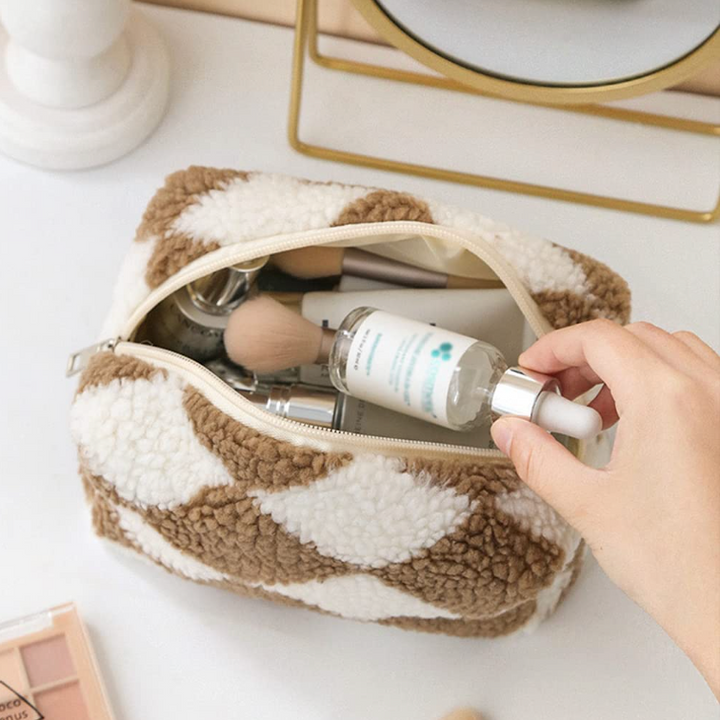 Borsa trucco in tessuto a scacchi beige e bianco, contenente pennelli e flacone di siero. Accessori cosmetici, beauty case elegante.