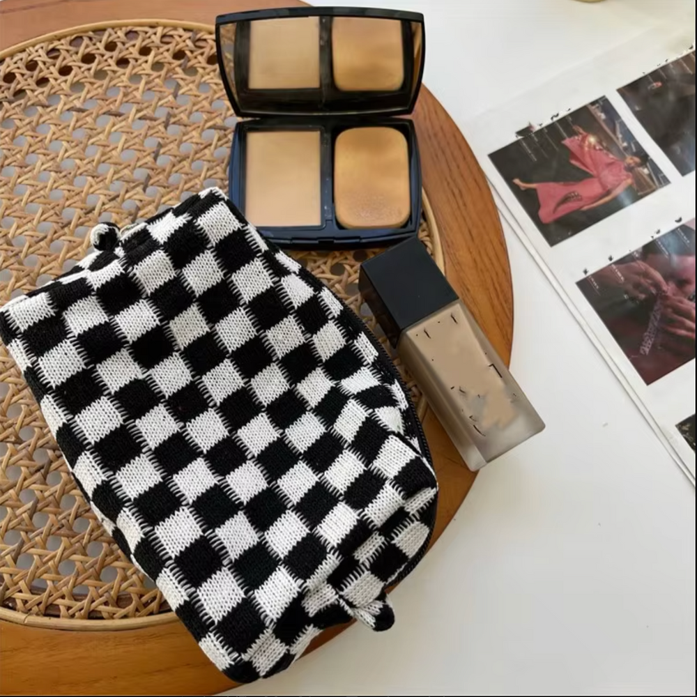 Trucco su tavolo: fondotinta liquido, cipria compatta aperta, fascia per capelli a scacchi bianca e nera. Accessori bellezza, cosmetici.