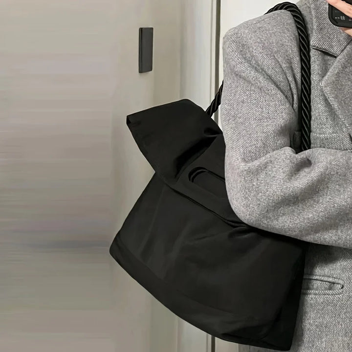 Borsa a spalla nera in tessuto, design elegante, manico intrecciato, indossata con cappotto grigio. Accessorio moda donna, stile casual chic.