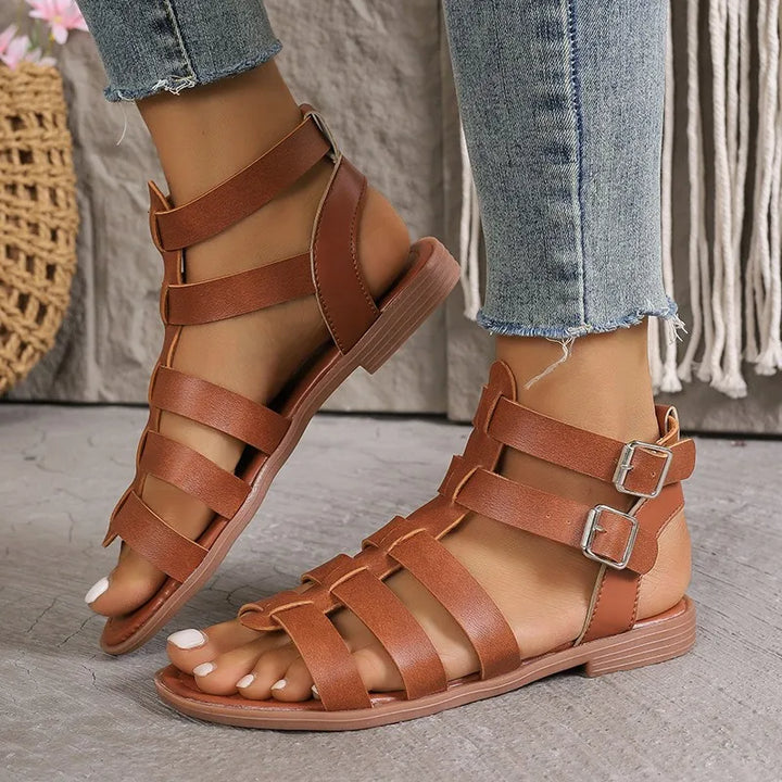 Sandali gladiatore in pelle marrone da donna, con fibbie doppie, indossati con jeans. Calzature estive eleganti e comode per un look casual.