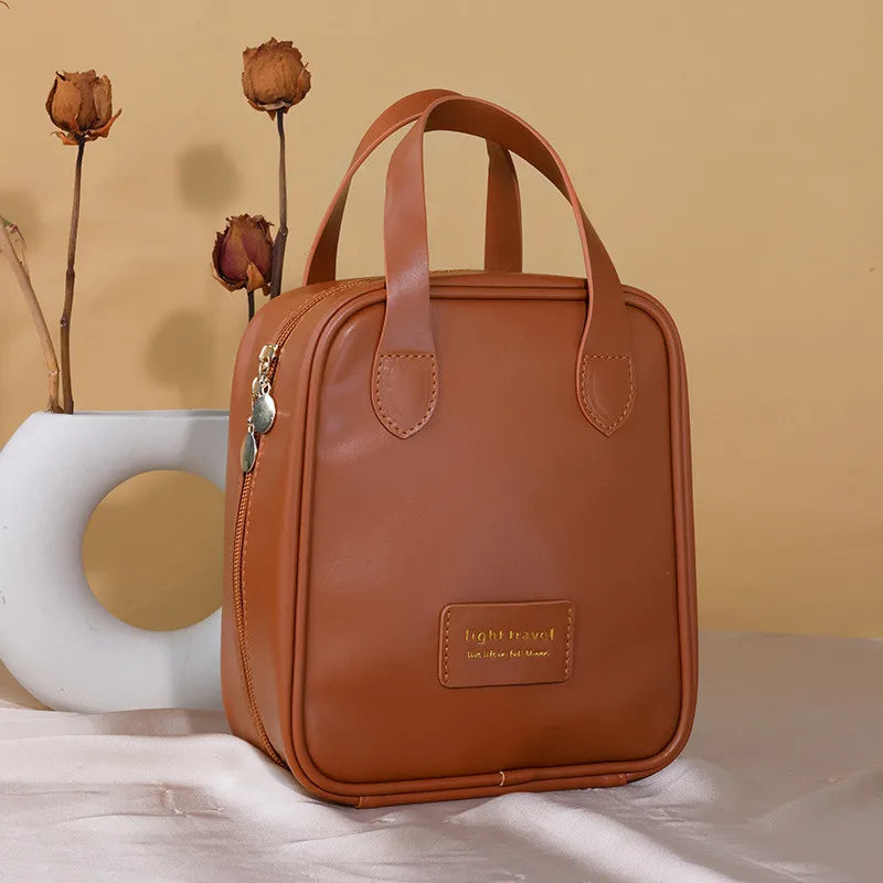 Borsa da viaggio in pelle marrone con manici, design elegante e compatto, sfondo beige con fiori secchi. Accessorio moda donna.