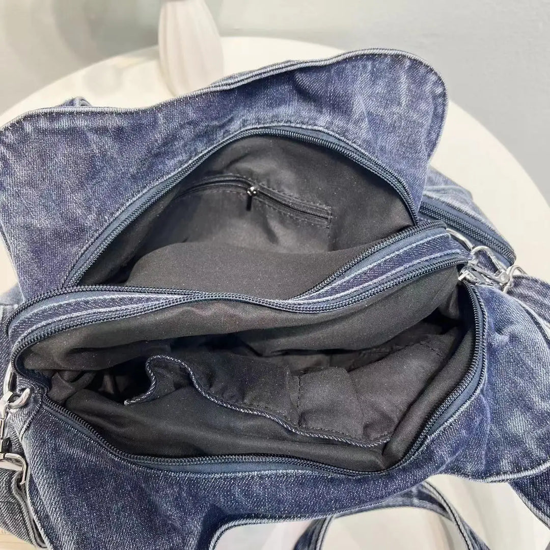 Borsa in denim blu aperta su tavolo bianco, con scomparti interni visibili. Design casual, ideale per moda quotidiana e accessori.
