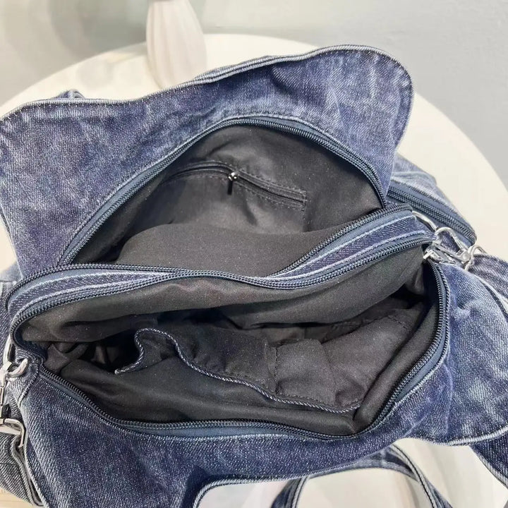 Borsa in denim blu aperta su tavolo bianco, con scomparti interni visibili. Design casual, ideale per moda quotidiana e accessori.