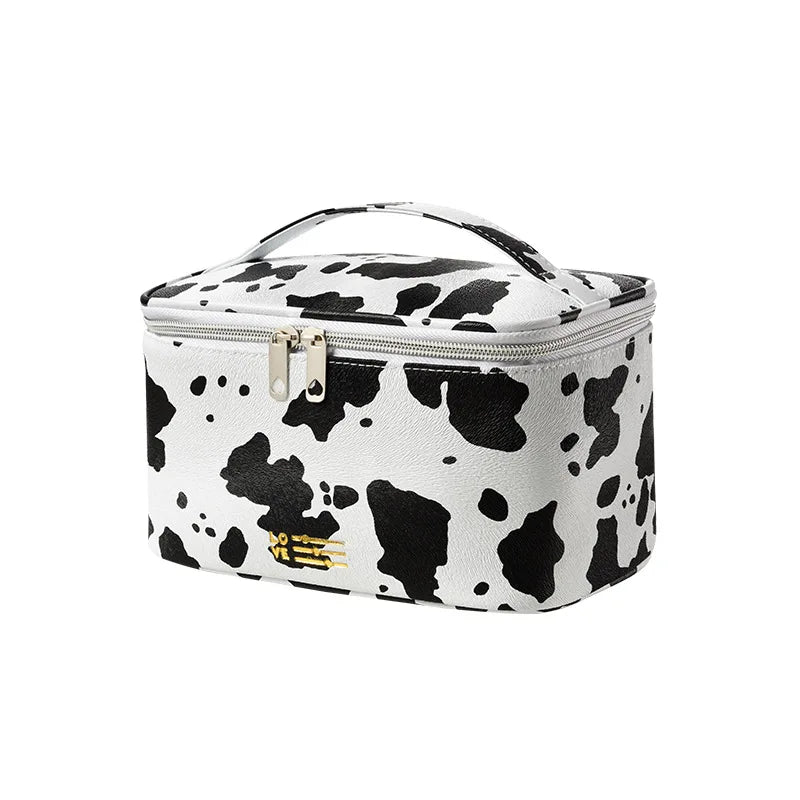 Astuccio cosmetico in ecopelle bianco e nero con stampa mucca, chiusura a zip e manico superiore. Design elegante e pratico per viaggi.