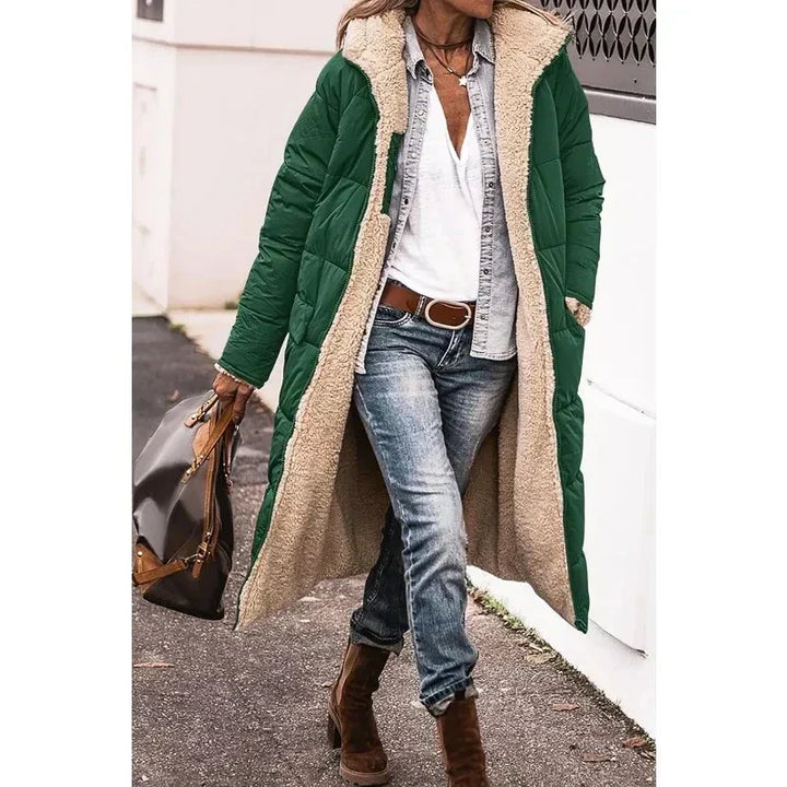 Cappotto lungo verde con fodera in pelliccia sintetica, indossato con jeans e stivali marroni. Moda invernale donna, stile casual chic.