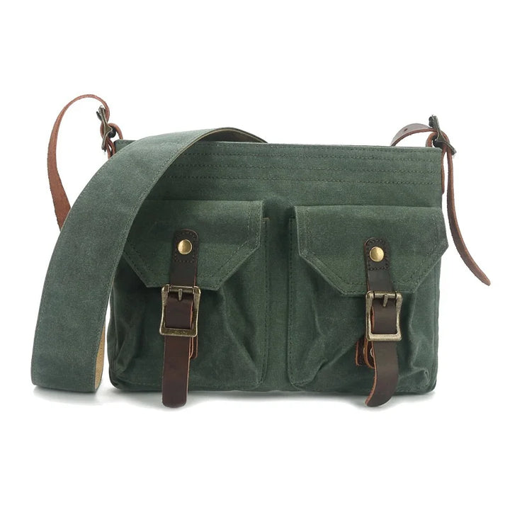 Borsa a tracolla verde in tela cerata con doppie tasche frontali e fibbie in pelle marrone. Design vintage, ideale per uomo e donna.