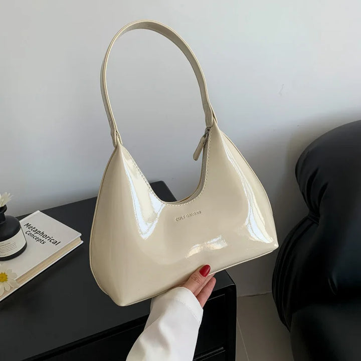 Borsa a spalla in pelle lucida beige, design moderno, manico singolo, su tavolo nero con decorazioni minimaliste. Accessorio moda elegante.