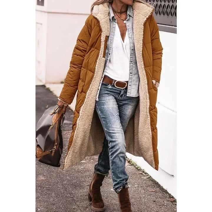 Cappotto lungo imbottito marrone donna, interno in pelliccia sintetica, abbinato a jeans e stivali marroni. Look casual autunnale.