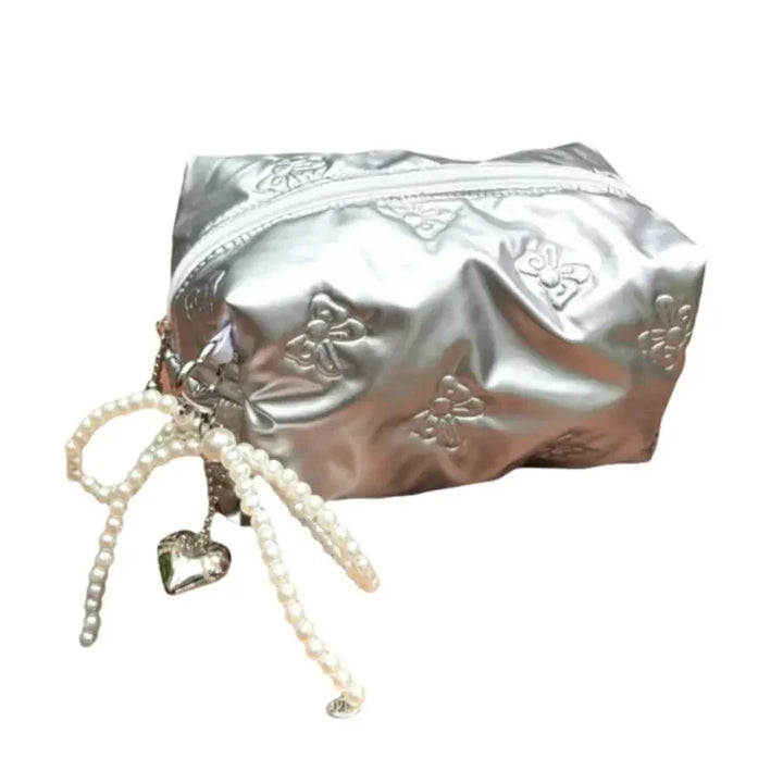 Astuccio cosmetico argento con cerniera, decorato con motivi floreali e pendente a cuore con perline. Elegante e pratico per trucco e accessori.