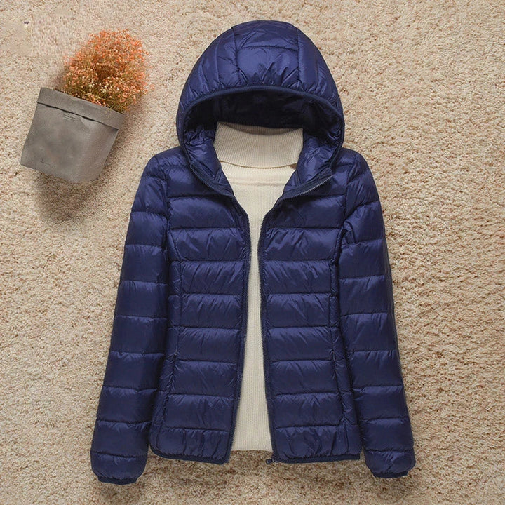 Giacca invernale donna blu con cappuccio, imbottita, su sfondo beige. Moda abbigliamento caldo, stile casual, ideale per freddo.