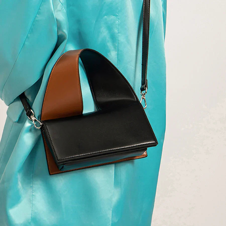 Borsa a tracolla in pelle nera e marrone su sfondo azzurro. Design moderno e minimalista, ideale per moda donna. Accessorio elegante e versatile.