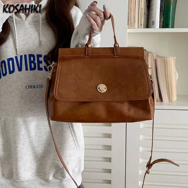 Borsa a mano in pelle marrone con tracolla regolabile, indossata da una donna in felpa grigia. Design elegante, ideale per moda casual e shopping.