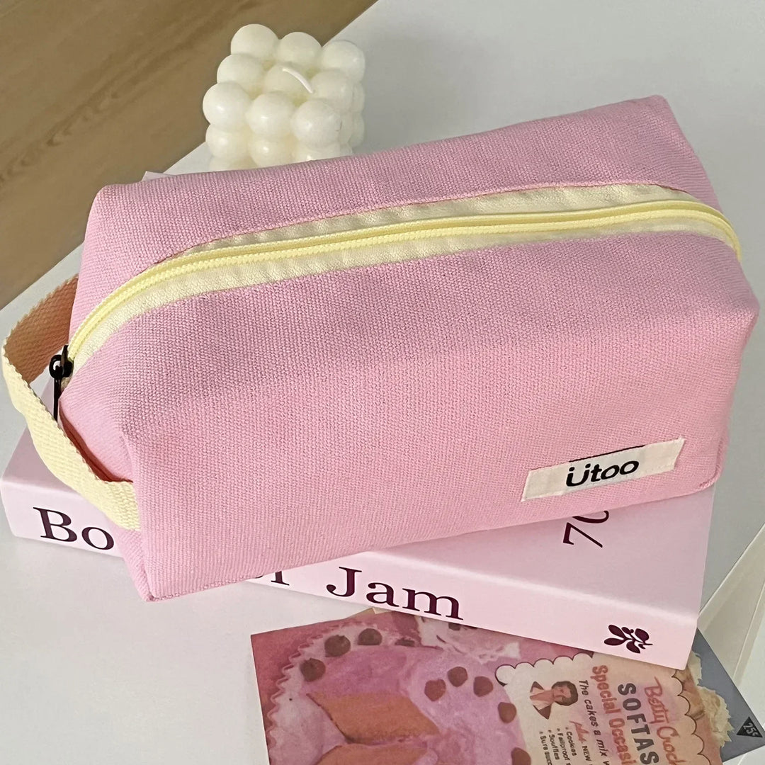 Astuccio rosa in tessuto con cerniera gialla, marchio "ütoo", su libri e decorazioni. Accessorio moda, organizzazione, scuola, viaggio.