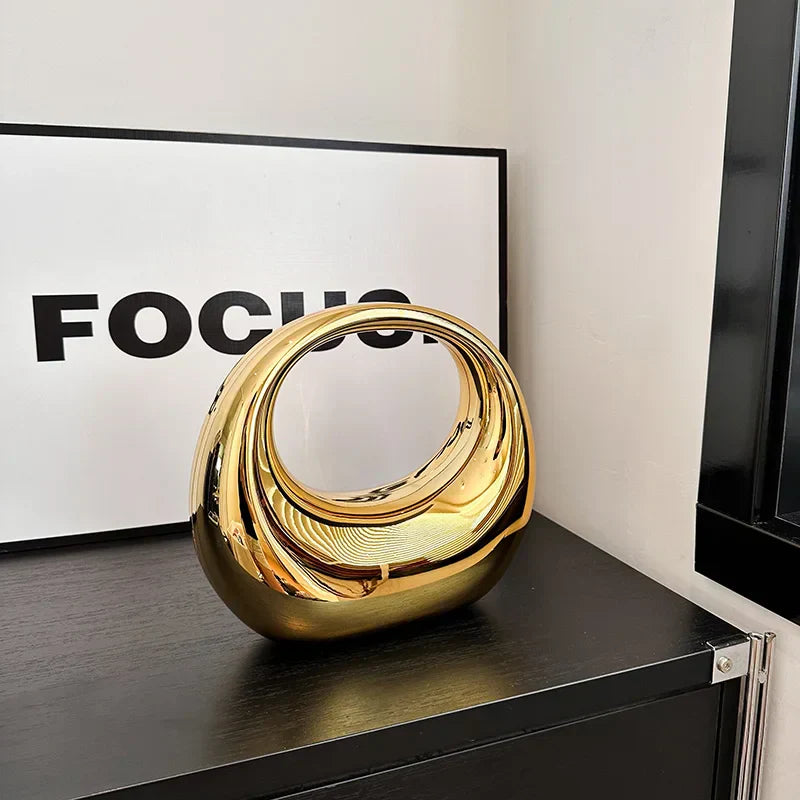 Scultura moderna in metallo dorato su tavolo nero, design astratto, decorazione d'interni elegante, accanto a quadro con scritta "FOCUS".