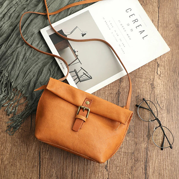 Borsa a tracolla in pelle marrone su tavolo di legno, accanto a rivista e occhiali. Accessorio moda elegante, perfetto per look casual e chic.