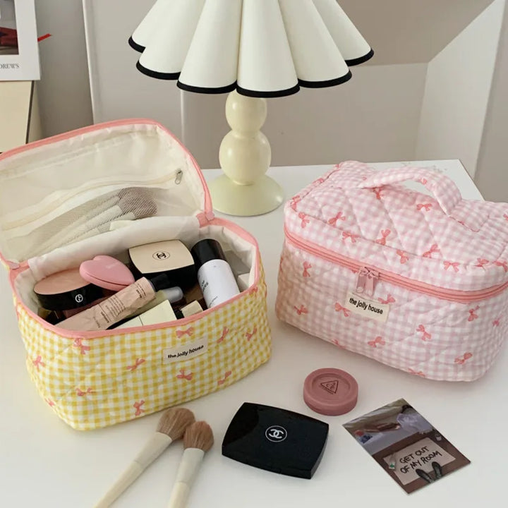 Due beauty case aperti su un tavolo bianco, contenenti trucchi e accessori cosmetici. Design a quadretti rosa e gialli. Lampada moderna sullo sfondo.