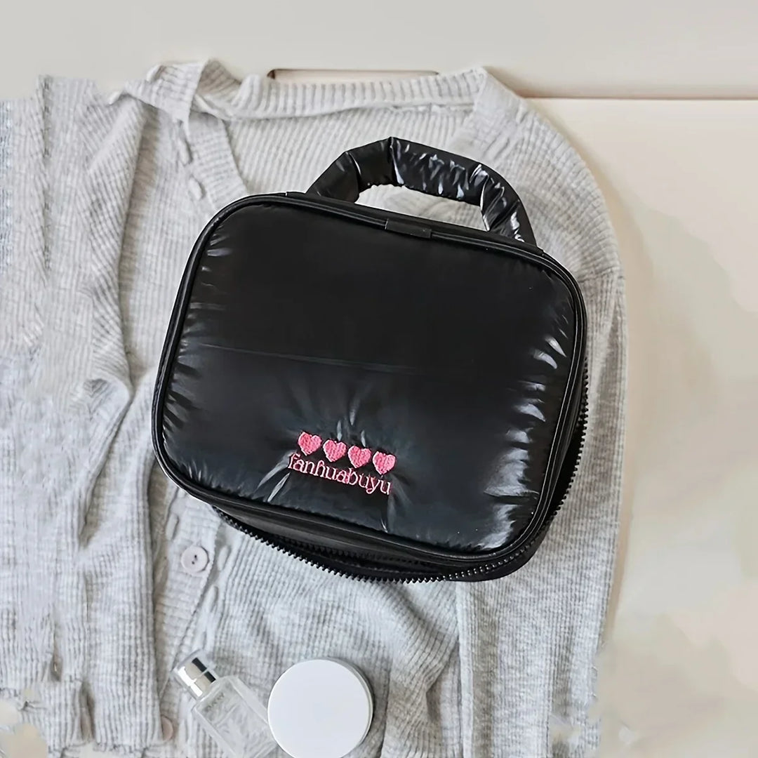 Borsa cosmetica nera su maglione grigio, con logo ricamato rosa. Ideale per viaggi, organizzazione trucco, accessori bellezza.