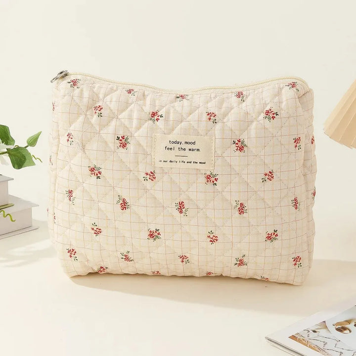 Borsa trapuntata beige con motivo floreale rosso, etichetta "today, mood feel the warm", su sfondo chiaro. Accessorio moda elegante e pratico.