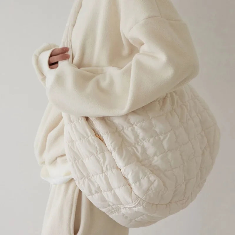 Borsa a tracolla trapuntata beige, indossata da una persona in abbigliamento coordinato chiaro. Accessorio moda elegante e versatile per ogni occasione.