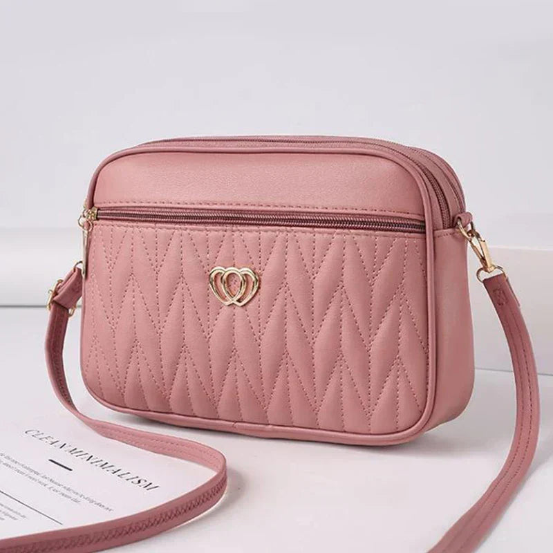 Borsa a tracolla rosa in pelle sintetica, design trapuntato a rombi, con cerniera e decorazione a cuore dorato. Elegante e moderna.