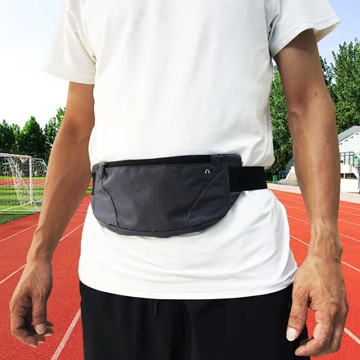 Marsupio sportivo grigio indossato da uomo su pista da corsa, ideale per jogging e attività all'aperto. Accessorio pratico e funzionale.