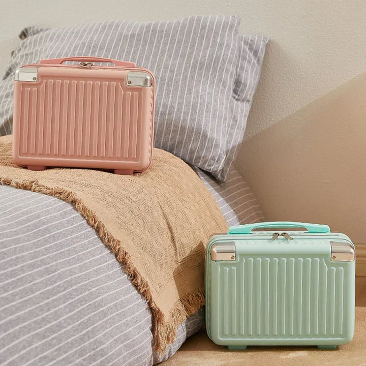 Due valigie rigide color pastello su letto con coperta beige e cuscini a righe. Design compatto, ideale per viaggi brevi e weekend.