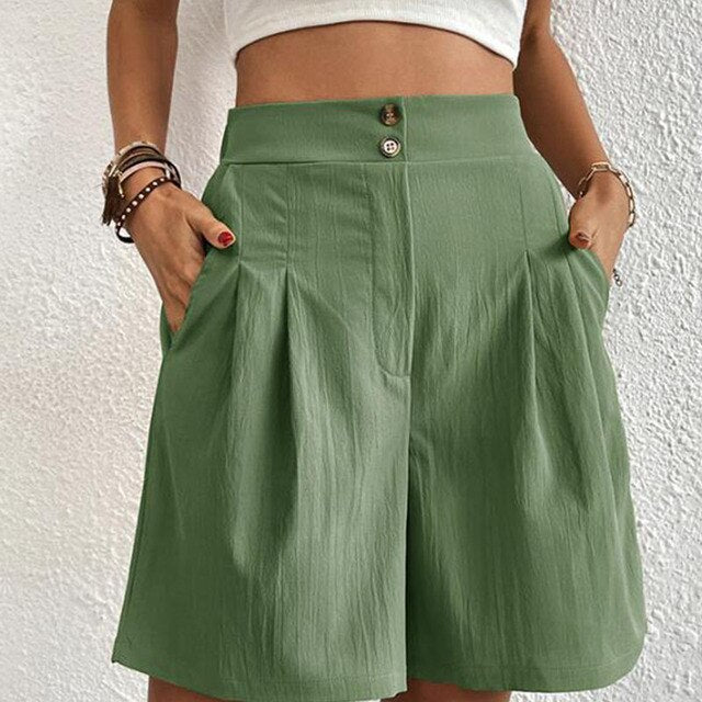 Shorts verdi da donna a vita alta con pieghe, tasche laterali e chiusura a bottone, indossati con top bianco. Moda estiva casual elegante.