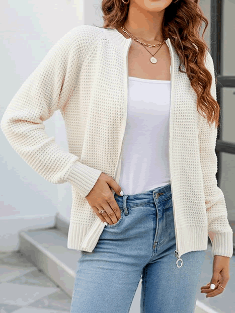Donna con cardigan bianco a maglia, zip frontale, indossa jeans blu e top bianco. Look casual elegante, moda autunnale femminile.