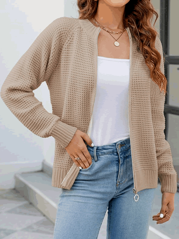 Donna con cardigan beige a maglia, top bianco e jeans blu. Moda casual autunnale, abbigliamento femminile elegante. Accessori: collane dorate.