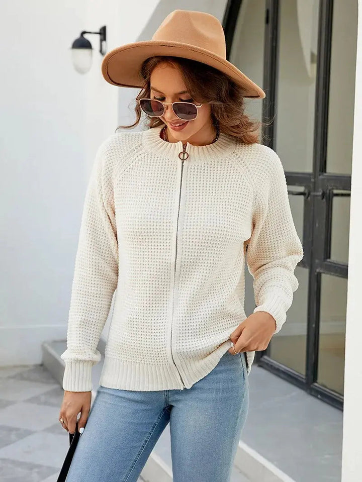 Donna con maglione bianco a zip, jeans azzurri, cappello marrone e occhiali da sole. Moda autunnale casual, outfit elegante per il tempo libero.